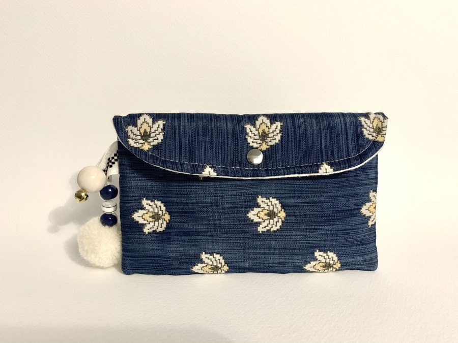 Clutch artesanal azul con flores de loto y pompón, hecho a mano en nuestro taller de costura